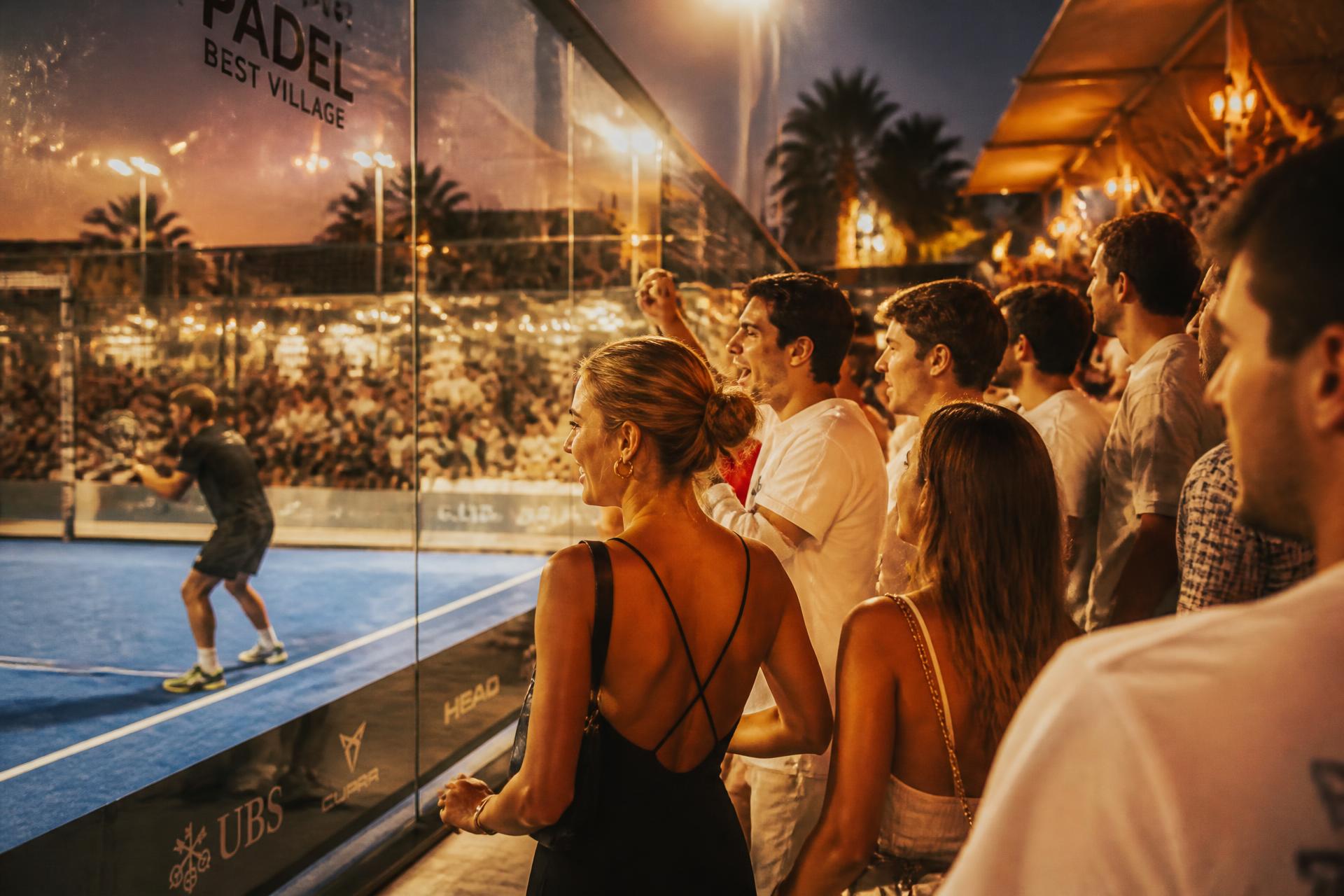 Publiek juicht langs de glazen wand tijdens een padeltoernooi in de avond